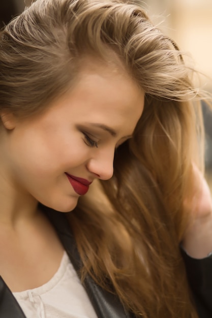 Gros plan d'une femme blonde souriante aux lèvres rouges et aux cheveux blonds luxuriants posant les yeux fermés