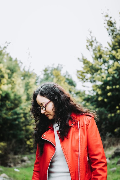 Gros plan d'une femme brune frisée souriante, vêtue d'une veste en cuir rouge dans un paysage froid