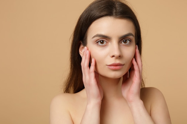 Gros plan sur une femme brune à moitié nue des années 20 avec une peau parfaite, maquillage nu isolé sur un mur pastel beige, portrait. Concept de procédures cosmétiques de soins de la peau.