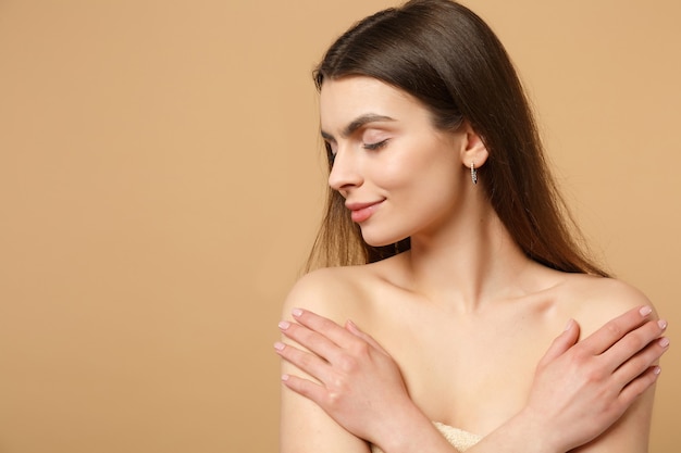 Gros plan sur une femme brune à moitié nue des années 20 avec une peau parfaite, maquillage nu isolé sur un mur pastel beige, portrait. Concept de procédures cosmétiques de soins de la peau.