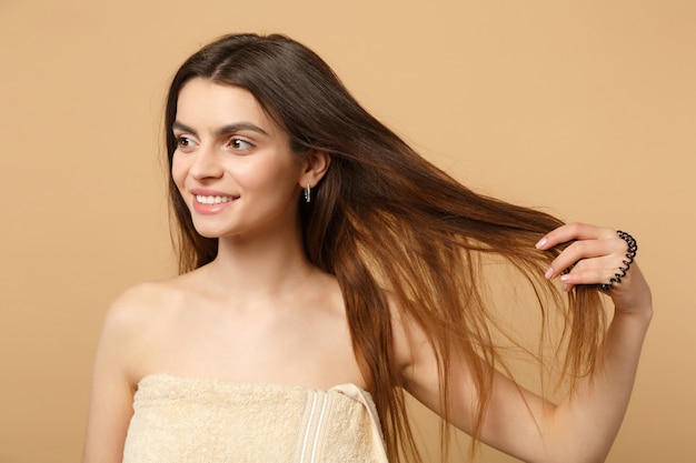 Gros plan sur une femme brune à moitié nue des années 20 avec une peau parfaite, maquillage nu isolé sur un mur pastel beige, portrait. Concept de procédures cosmétiques de soins de la peau.