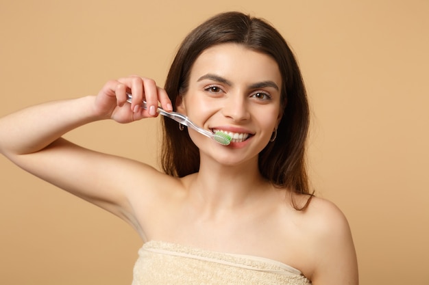 Gros plan sur une femme brune à moitié nue avec une peau parfaite, une brosse de maquillage nue isolée sur un mur pastel beige