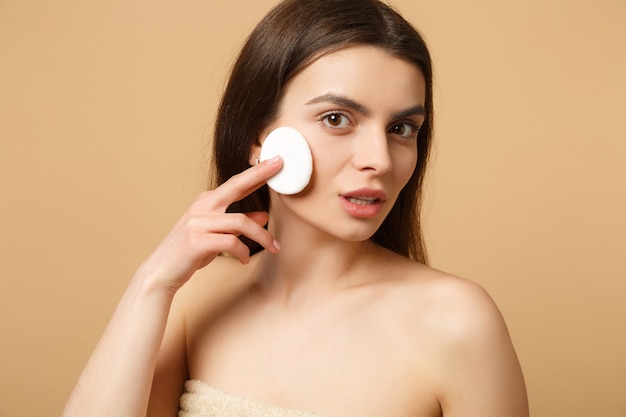 Gros plan femme brune à moitié nue avec une peau parfaite, maquillage nu isolé sur un mur pastel beige