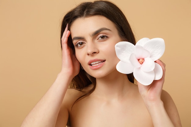 Gros plan femme brune à moitié nue avec une peau parfaite, maquillage nu isolé sur un mur pastel beige