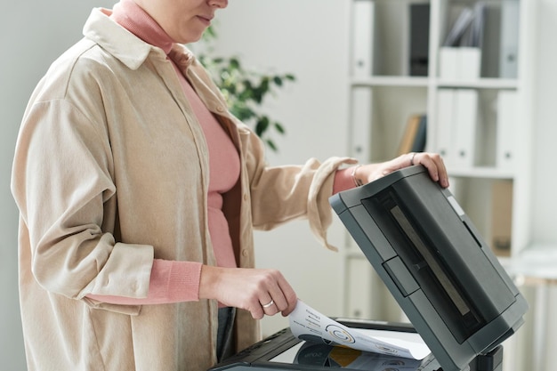 Gros plan d'une femme de bureau en chemise beige à l'aide d'un scanner tout en faisant une copie du document