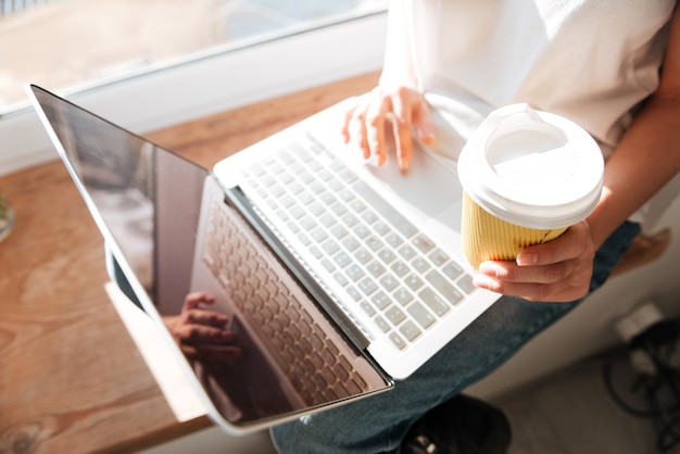 Gros plan d'une femme buvant du café et utilisant un ordinateur portable à écran blanc