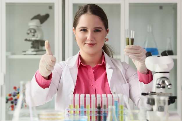 Gros plan d'une femme chimiste tenant des tubes à essai et montrant les pouces vers le haut signe l'enseignement des sciences