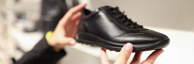 Gros plan d'une femme choisissant une sneaker noire dans un magasin de chaussures femme tenant une botte élégante dans les mains nouveau