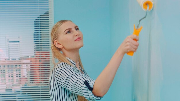 Gros plan d'une femme constructeur sur un chantier de construction avec un rouleau à peinture travaillant sur un mur de peinture avec...