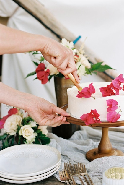 Gros plan d'une femme coupant un gâteau avec du glaçage blanc et décoré de fleurs rouges