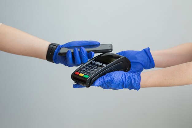 Gros plan d'une femme dans des gants applique un smartphone à un terminal effectuant un paiement sans contact réussi. Client effectuant un paiement sans contact pour utiliser le paiement par smartphone, technologie NFC.