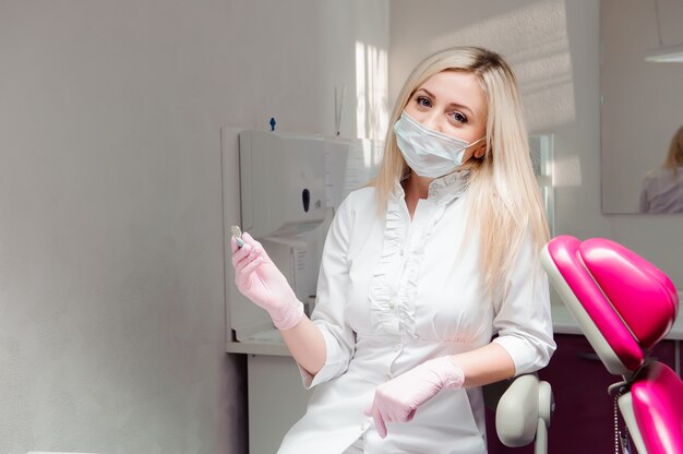 Gros plan d'une femme dentiste au masque avec des outils.