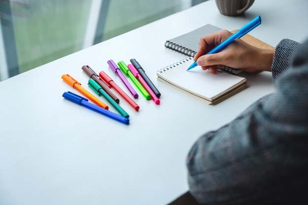 Gros plan d'une femme écrivant sur un cahier vierge avec des stylos de couleur sur la table