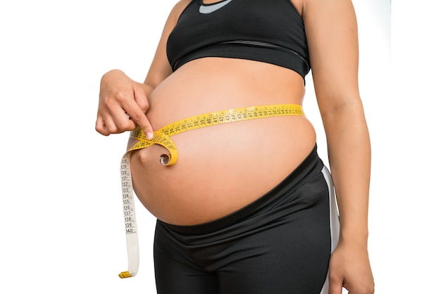 Gros plan d'une femme enceinte à l'aide d'un ruban à mesurer pour vérifier le développement du bébé. Concept de grossesse et de maternité.