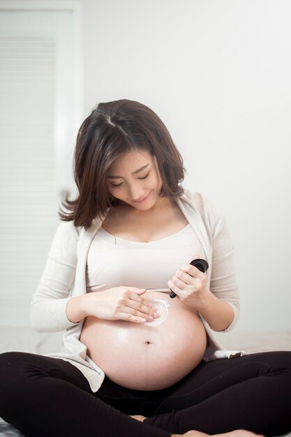 Gros plan d&#39;une femme enceinte en appliquant la crème sur son ventre