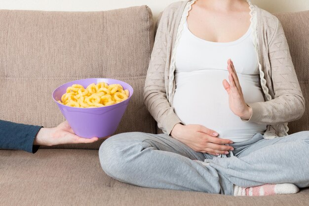 Gros plan d'une femme enceinte assise sur le canapé refuse de manger des collations malsaines Arrêtez-vous à la malbouffe pendant la grossesse concept