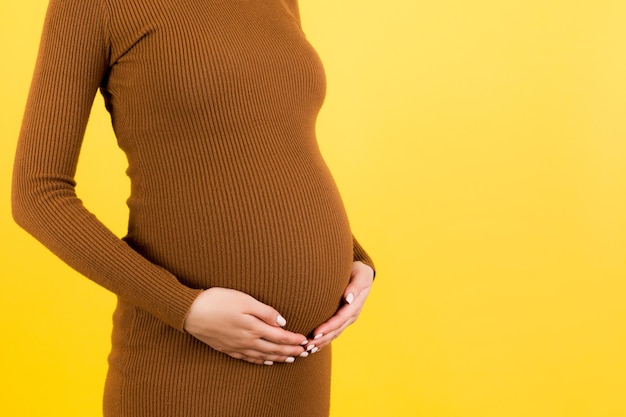 Gros plan sur une femme enceinte en robe marron tenant son ventre sur fond jaune Concept de maternité Espace de copie