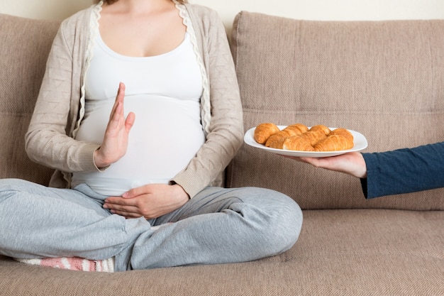 Gros plan d'une femme enceinte se détendre sur le canapé fait un geste d'arrêt aux croissants