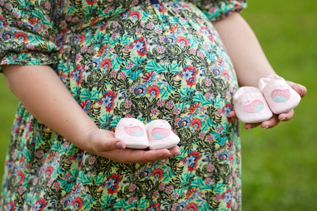 Gros Plan D'une Femme Enceinte Tenant Des Chaussures De Bébé Sur Son Ventre. Jumeaux