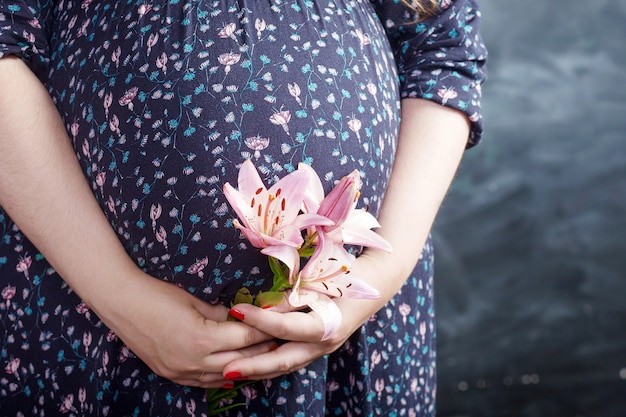 Photo gros plan d'une femme enceinte tenant une fleur et toucher son ventre