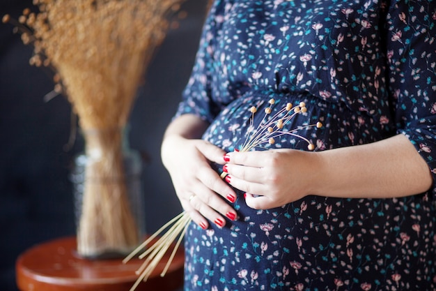 Gros plan d'une femme enceinte tenant une fleur et toucher son ventre