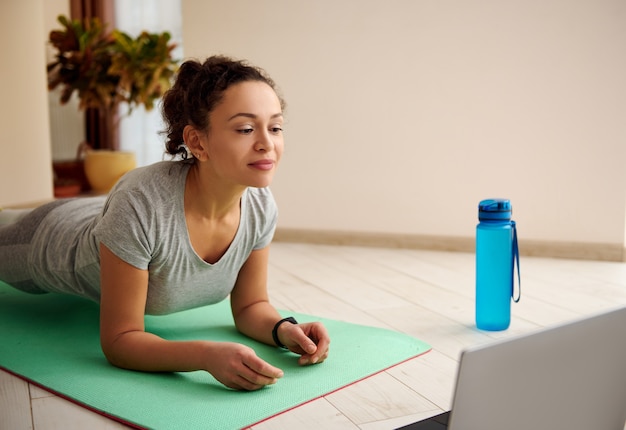 Gros plan d'une femme faisant des exercices de planche tout en regardant des tutoriels de remise en forme sur ordinateur portable. Fitness en ligne pendant le verrouillage pandémique