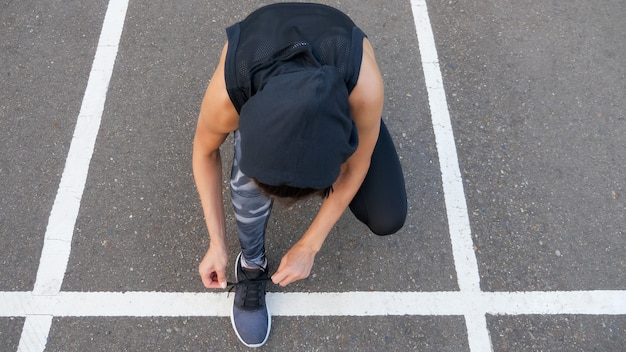 Gros plan sur une femme en forme attachant des lacets en se tenant debout sur une route goudronnée pendant le jogging en soirée d'été