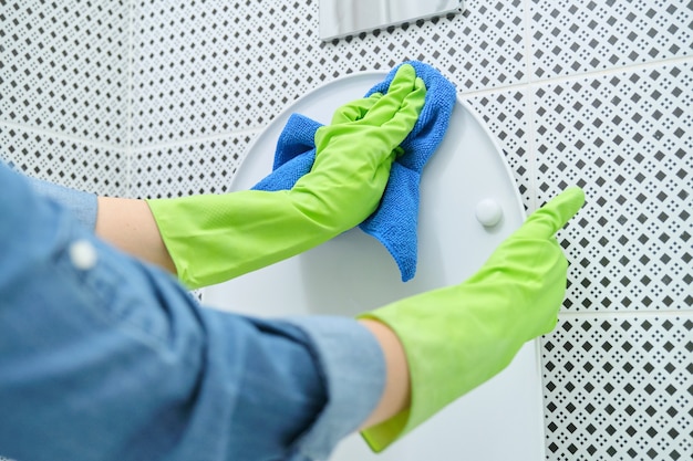 Gros plan sur une femme en gants avec un chiffon et un détergent pour nettoyer la cuvette des toilettes, nettoyage à domicile dans la salle de bain