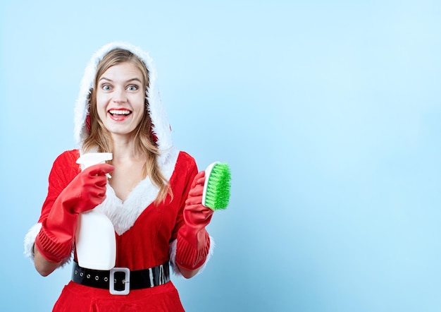 Gros plan d'une femme heureuse caucasienne portant des vêtements de père noël et des gants de nettoyage tenant un spray de nettoyage et une brosse