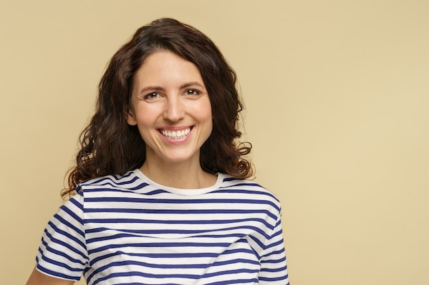 Gros plan d'une femme heureuse avec un maquillage naturel, une peau saine, des cheveux bouclés, un sourire à pleines dents blanc isolé