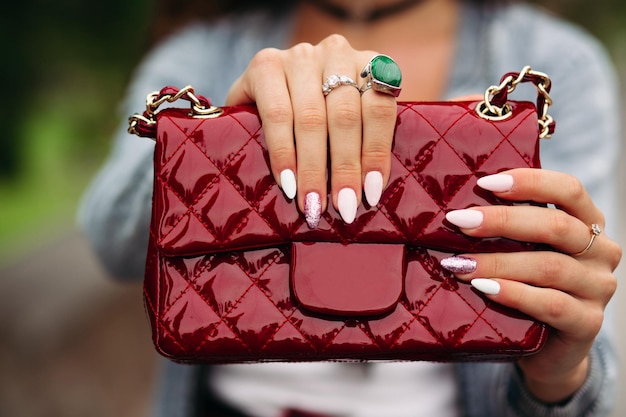 Gros plan d'une femme incognito avec manucure élégante portant des bijoux tenant un joli petit sac rouge.