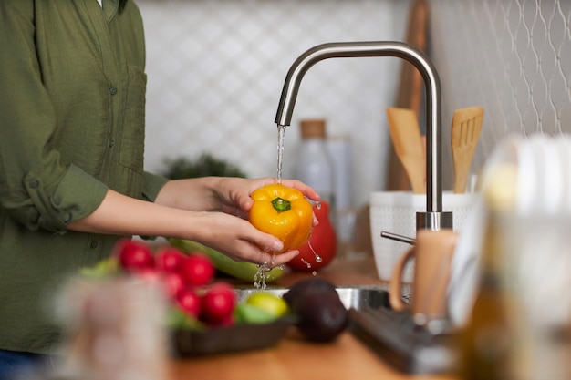 Gros plan sur une femme lavant des légumes mûrs frais dans la cuisine