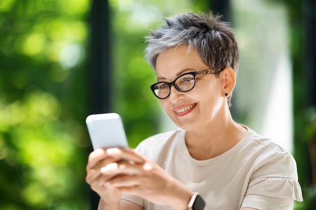 Gros plan d'une femme mature heureuse utilisant un téléphone portable sur le lieu de travail