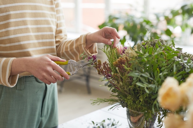 Gros plan sur une femme méconnaissable coupant des plantes tout en organisant des compositions florales en atelier, espace de copie