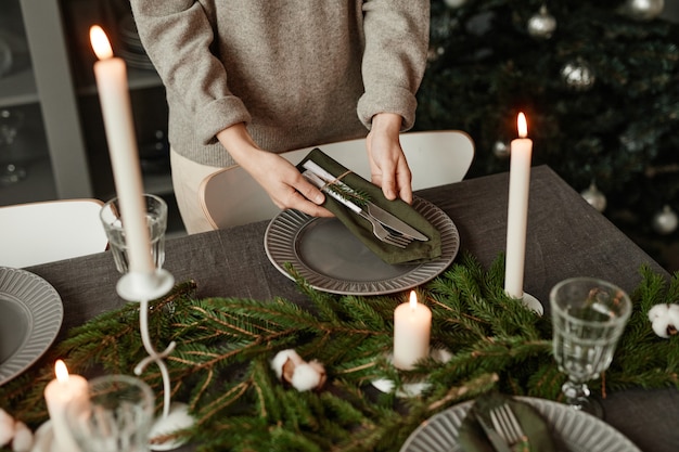 Gros plan d'une femme méconnaissable installant une table à manger pour Noël décorée de branches de sapin et...