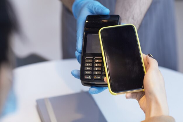 Gros plan d'une femme méconnaissable payant via un smartphone NFC dans un café avec des mesures de sécurité covid, espace de copie