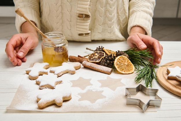 Gros plan sur une femme méconnaissable préparant des biscuits au pain d'épice, les saupoudrant de sucre en poudre pour Noël.