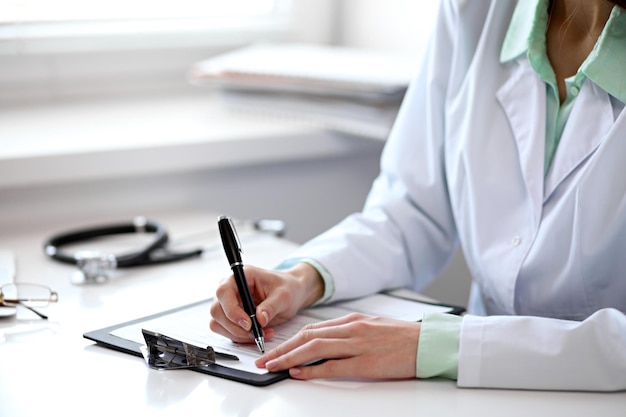 Gros plan d'une femme médecin inconnue assise à la table près de la fenêtre à l'hôpital et tapant sur un ordinateur portable