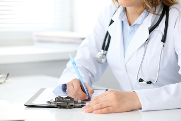 Gros plan d'une femme médecin inconnue assise à la table près de la fenêtre à l'hôpital et tapant sur un ordinateur portable