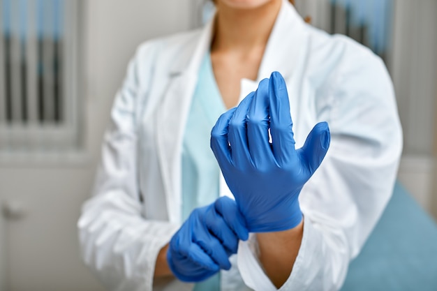 Gros plan d'une femme médecin mettant un gants en latex bleu sur un fond de clinique