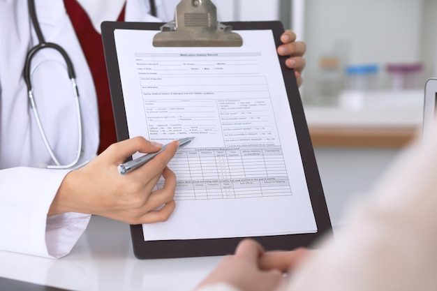 Gros plan d'une femme médecin pointant vers un formulaire de demande tout en consultant le patient