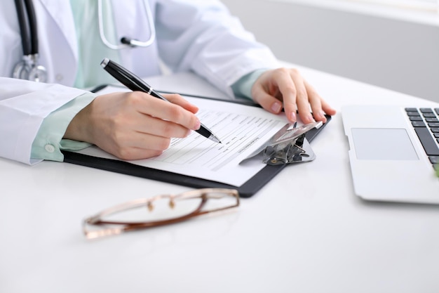 Gros plan d'une femme médecin remplissant un formulaire de demande, assise à la table de l'hôpital