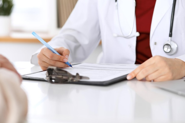 Gros plan d'une femme médecin remplissant un formulaire de demande tout en consultant le patient