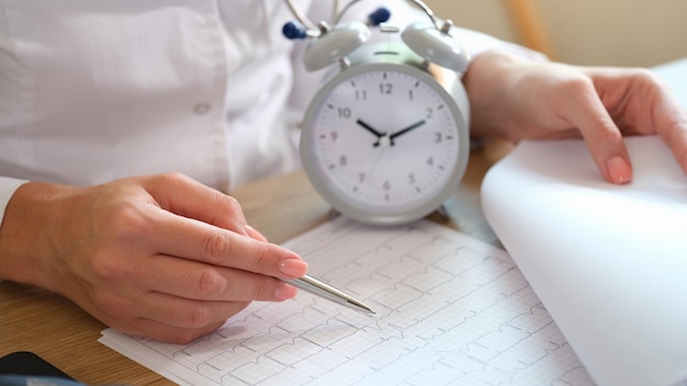 Photo gros plan d'une femme médecin avec réveil et cardiogramme à l'heure du bureau de l'hôpital pour des raisons médicales