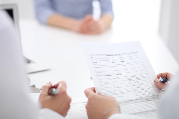 Gros plan d'une femme médecin tenant un formulaire de demande tout en consultant le patient.