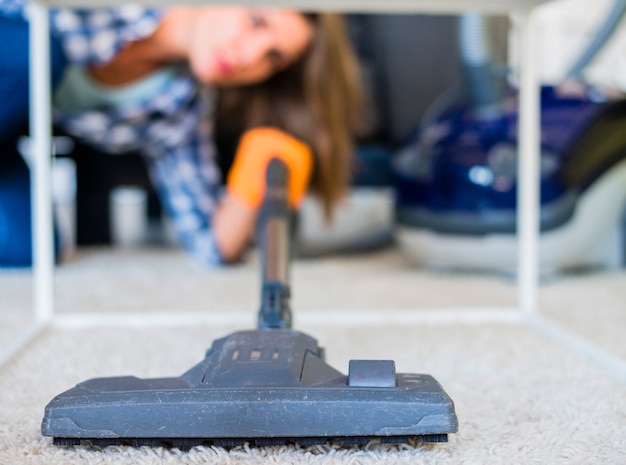 Photo gros plan d'une femme de ménage nettoyant un tapis avec un aspirateur