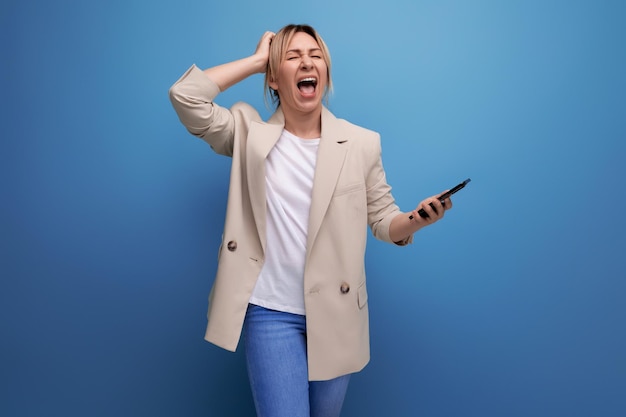 Gros plan d'une femme millénaire blonde hurlante bouleversée dans une veste avec un smartphone sur un studio