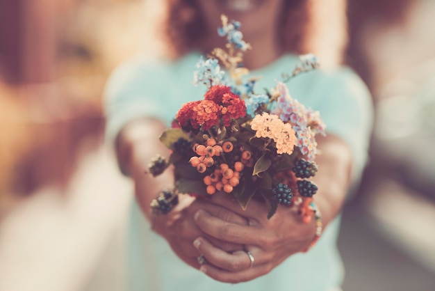 Gros plan sur une femme montrant un bouquet floral naturel printanier dans un filtre de tons pastel. Fleurs de fleurs et concept de cadeau actuel.