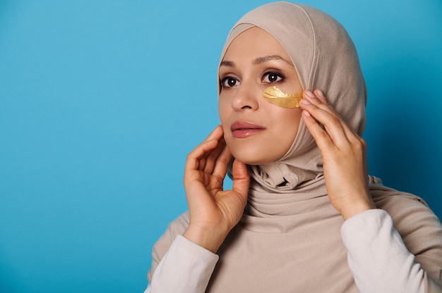 Gros plan d'une femme musulmane en hijab à l'aide de patchs oculaires hydrogel. Portrait de beauté