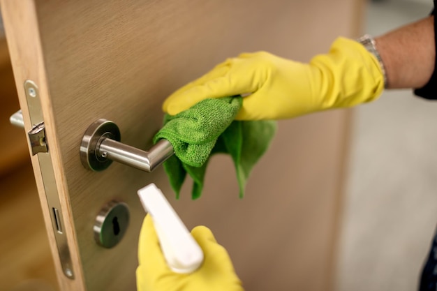 Gros plan sur une femme nettoyant la poignée de porte avec un désinfectant